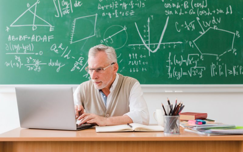 nauczyciel siedzący przy biurku pisze na klawiaturze, laptop dla nauczyciela